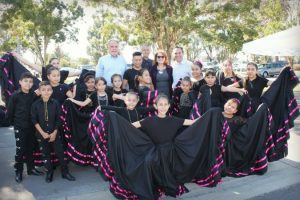 Group of children dressed in traditional black dresses with pink accents standing outdoors together.
