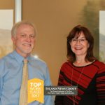 Smiling man and woman standing together indoors near large window with mountain view.