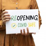 Person holding sign reading "Reopening COVID Safe" with checkmark symbol.