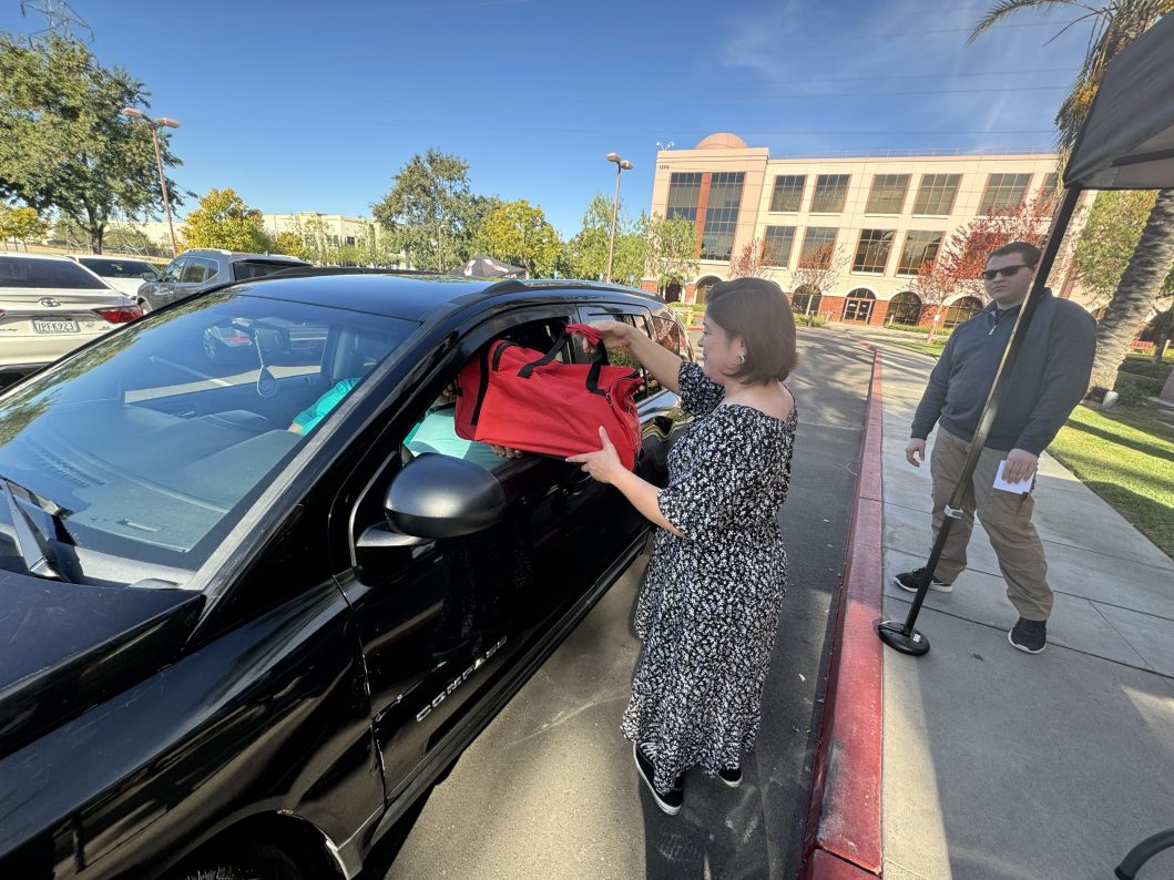 Woman placing red bag through black car window, man standing nearby holding papers.