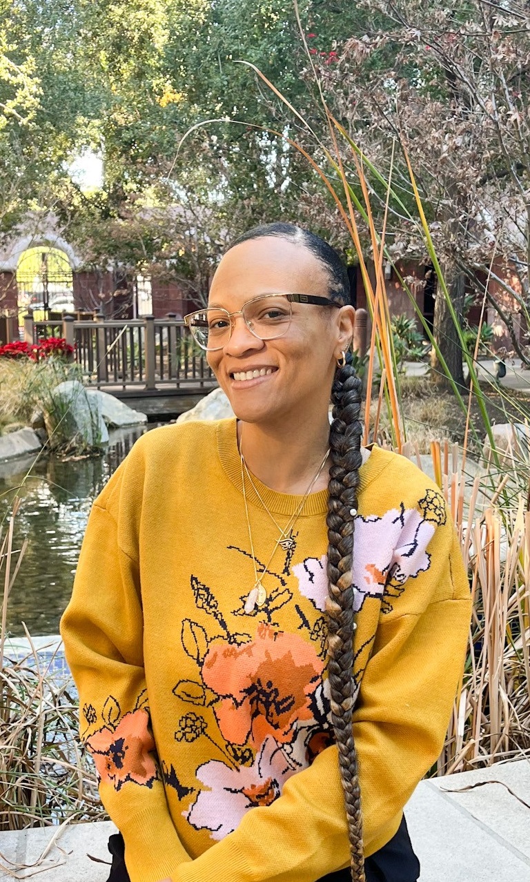 A picture of IRC Employment Specialist Krystal Spear sitting in front of a pond and wearing a yellow sweater