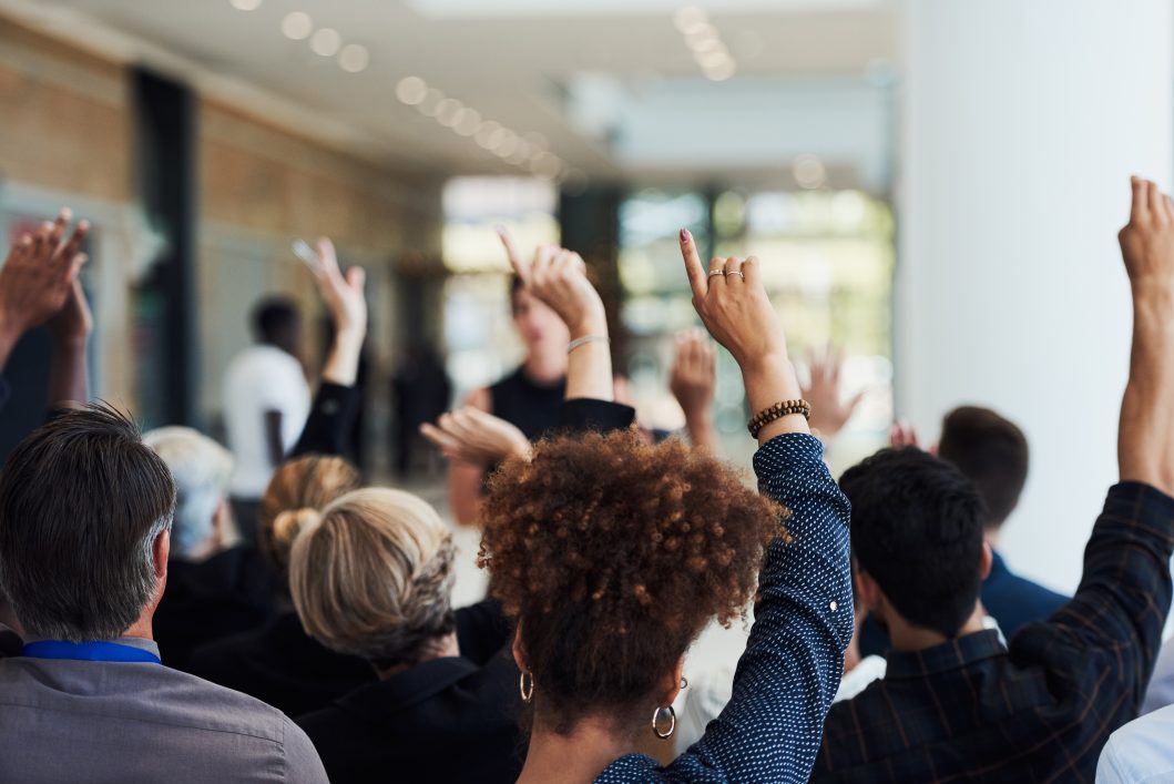 Audience members raising hands in a conference hall with blurred background.