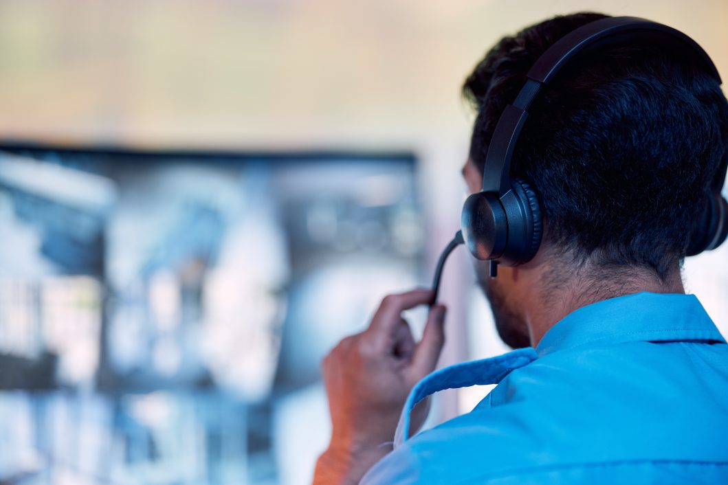 Person wearing headset in blue shirt, facing computer monitor with blurred images.