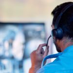 Person wearing headset in blue shirt, facing computer monitor with blurred images.