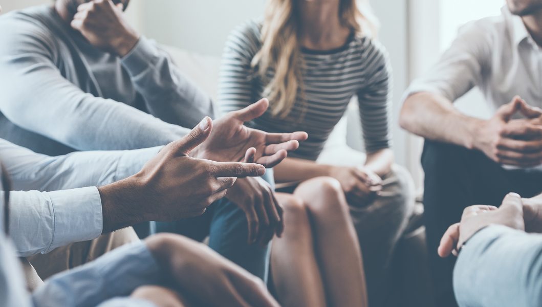 People sitting in a circle engaging in a group discussion, gesturing and listening attentively.