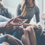 People sitting in a circle engaging in a group discussion, gesturing and listening attentively.