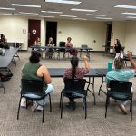 Classroom with diverse group engaged in sign language, instructor leading color activity on screen.