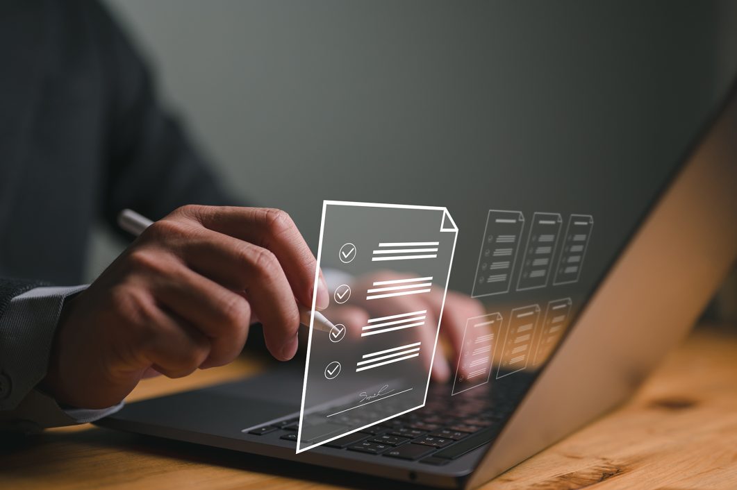 Hands holding stylus touching virtual checklist on open laptop with digital documents.