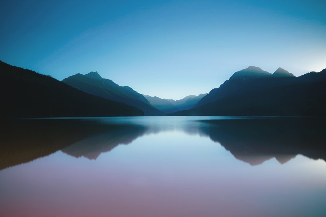 Mountain landscape reflected on still lake under clear blue sky at dusk.
