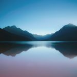 Mountain landscape reflected on still lake under clear blue sky at dusk.