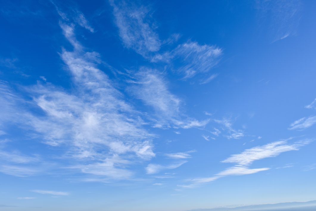 Blue sky with scattered wispy white clouds on a clear sunny day.
