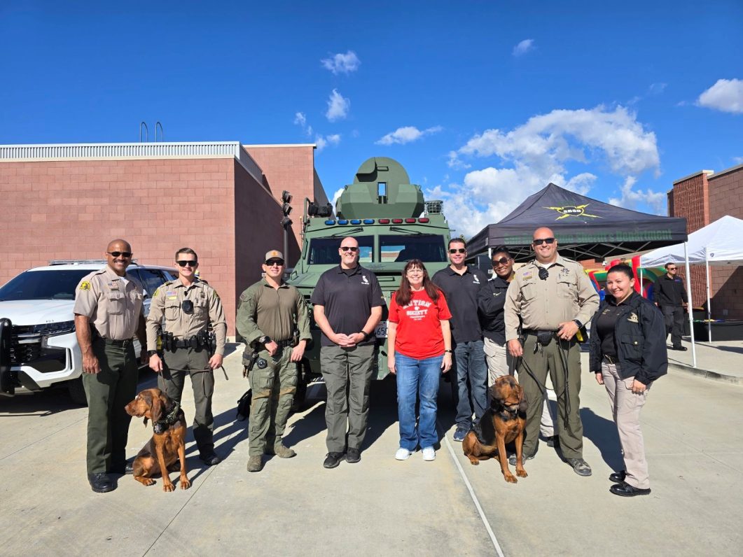 Group of people and two dogs in front of armored vehicle and tents under clear sky