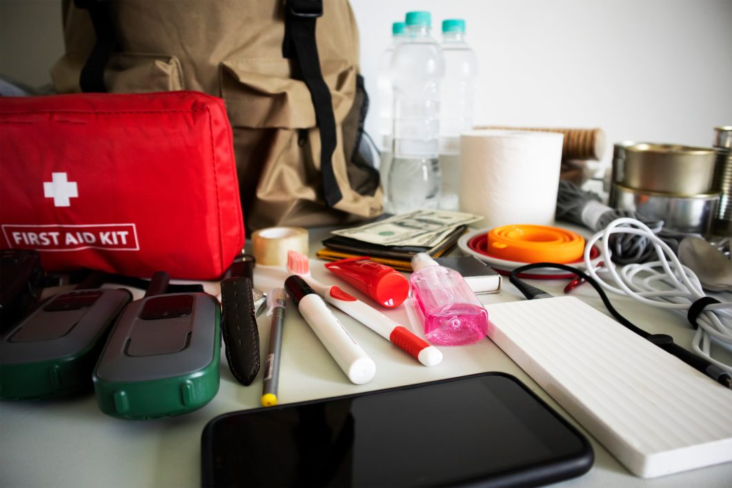 Emergency preparedness kit including first aid, bottled water, flashlight, cash, and snacks on table.