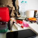 Emergency preparedness kit including first aid, bottled water, flashlight, cash, and snacks on table.