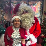 Elderly woman with Santa Claus in festive setting, surrounded by Christmas decorations and tree.