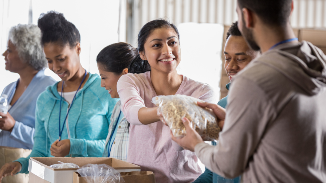 Smiling woman handing bag of cereal to volunteer at community food distribution event.