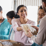 Smiling woman handing bag of cereal to volunteer at community food distribution event.