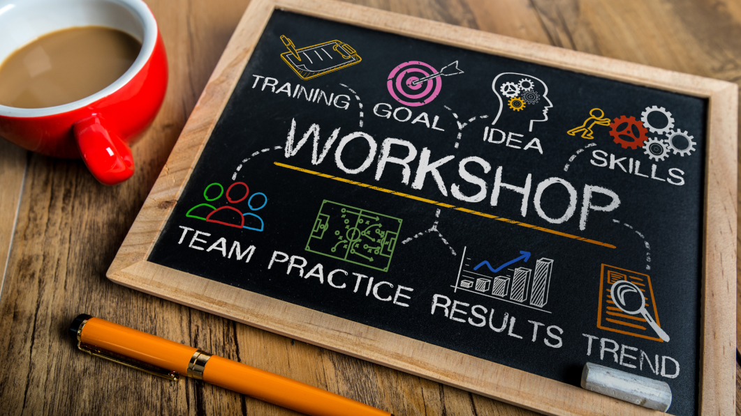 Chalkboard with workshop terms, colorful icons, red coffee cup, orange pen on wooden table.