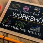 Chalkboard with workshop terms, colorful icons, red coffee cup, orange pen on wooden table.