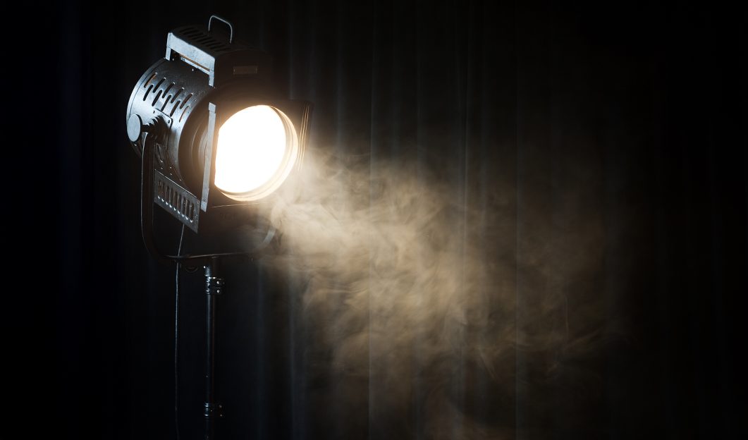 Black stage spotlight emitting bright beam with visible mist or smoke in dark setting.