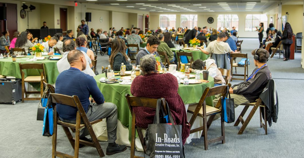 People sitting around tables with green tablecloths at a conference or meeting event.