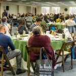 People sitting around tables with green tablecloths at a conference or meeting event.