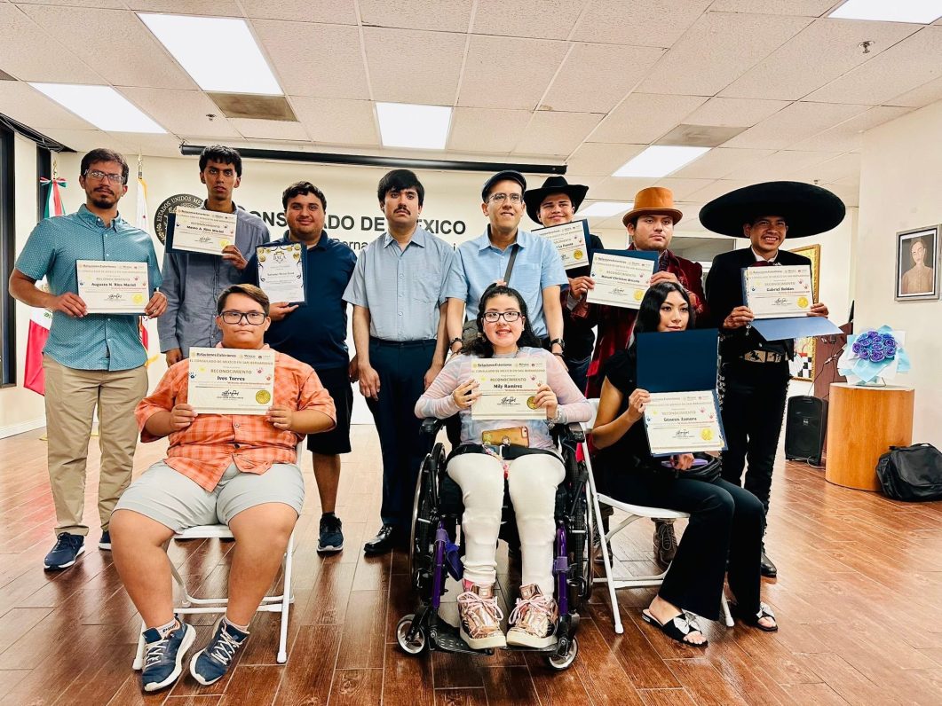 Group of eleven people holding certificates, some seated, smiling in a room with wooden floor.