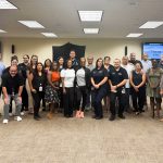 Large diverse group of people posing for photo in conference room, smiling at camera.