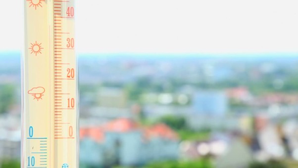 Outdoor thermometer showing temperature, colorful cityscape blurred in background, indicating sunny weather.