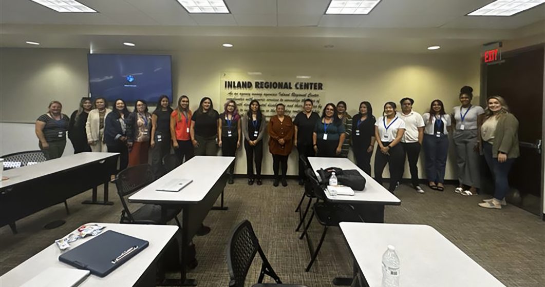 Group of people standing in conference room with tables, facing camera, Inland Regional Center sign.