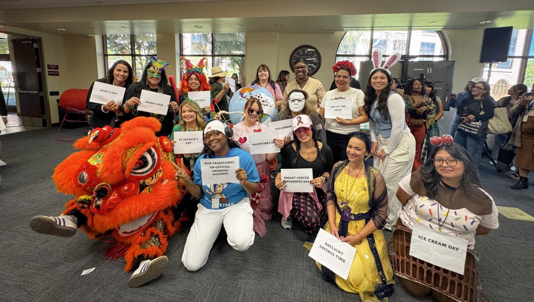 Group of people in colorful costumes holding signs for various holidays, standing indoors.