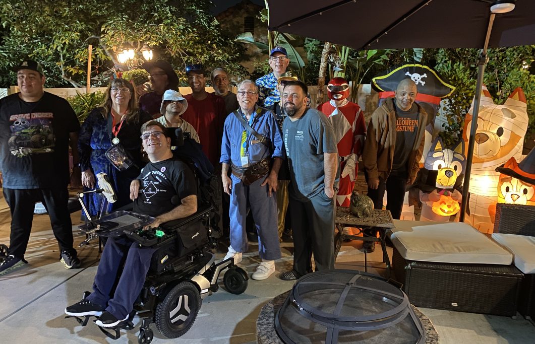 Group of people in casual clothes and costumes outdoors at night, with Halloween decorations.