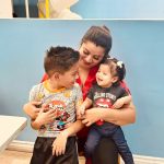 Woman in red shirt with two smiling children against blue wall indoor setting.