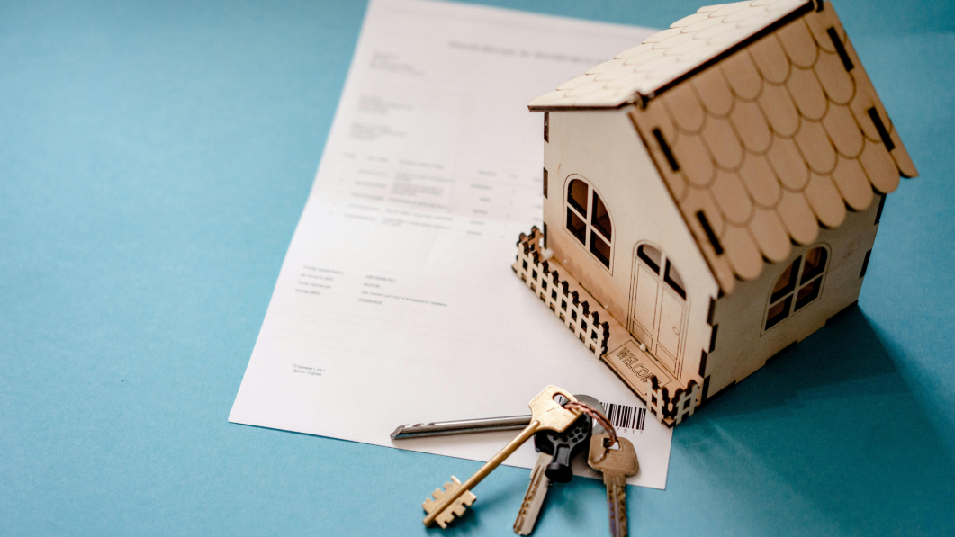 Wooden house model and keys on top of a document, blue background.