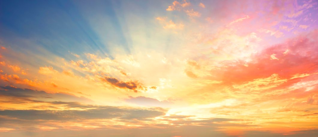 Vibrant sunset sky with golden clouds and sun rays streaming through colorful horizon.