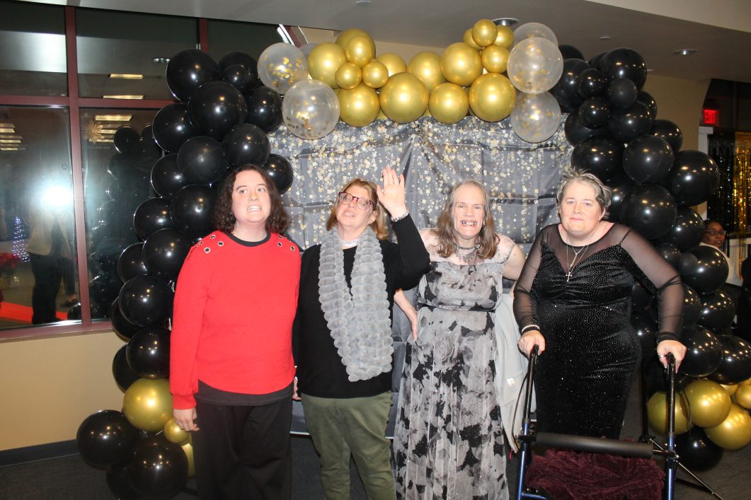 Four women posing in front of balloon arch decoration.