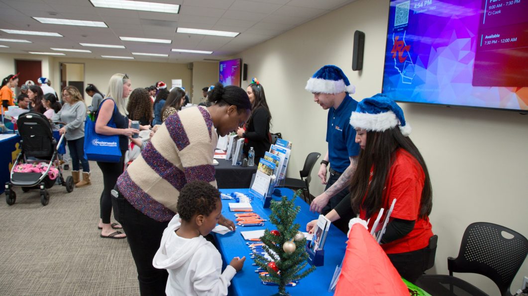 Crowded holiday-themed event with attendees exploring vendor tables.