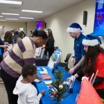 Crowded holiday-themed event with attendees exploring vendor tables.
