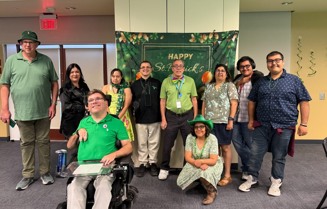 Group photo of attendees posing in front of a St. Patrick’s Day backdrop at an IRC community event.