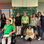 Group photo of attendees posing in front of a St. Patrick’s Day backdrop at an IRC community event.