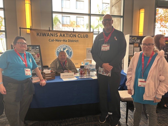 Group photo in front of a Kiwanis Aktion Club booth at an event