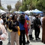 Crowds gathered along a street lined with vendor tents and booths during the Autism Acceptance Walk, including attendees in costumes and community members exploring the event.