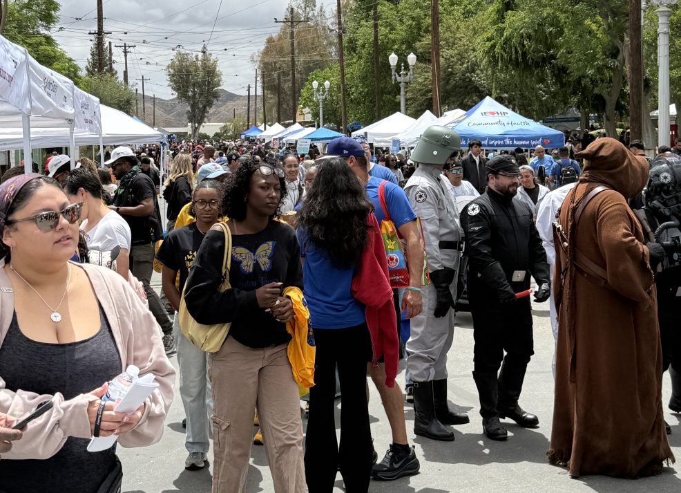Crowds gathered along a street lined with vendor tents and booths during the Autism Acceptance Walk, including attendees in costumes and community members exploring the event.