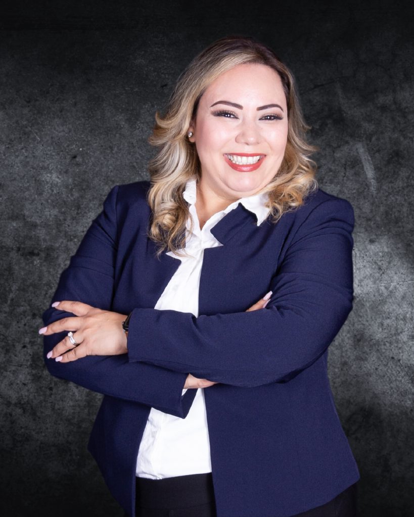 A picture of IRC Cultural Specialist Mari Rodriguez wearing a blue jacket, white shirt, and smiling