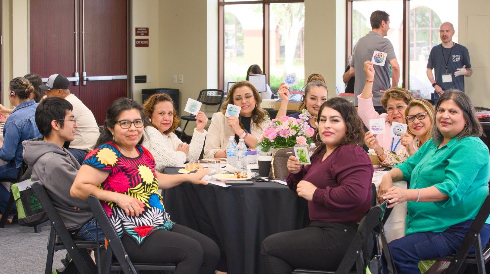 Conference attendees seated around a table holding activity cards and participating in a group wellness activity during the Service, Access and Equity Conference.
