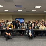 Group photo of panelists and attendees gathered in a conference room during an autism acceptance month event.