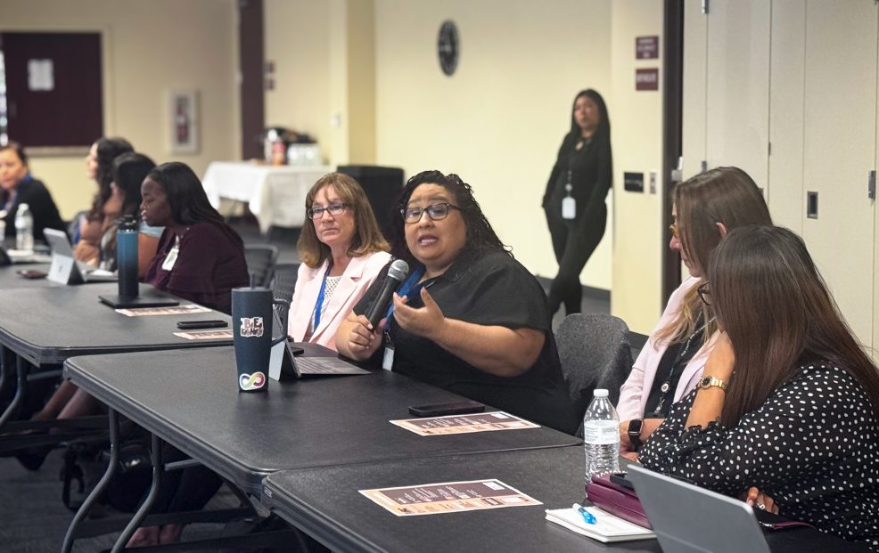 Participant speaking into a microphone during a Native American coalition meeting while attendees listen around conference tables.