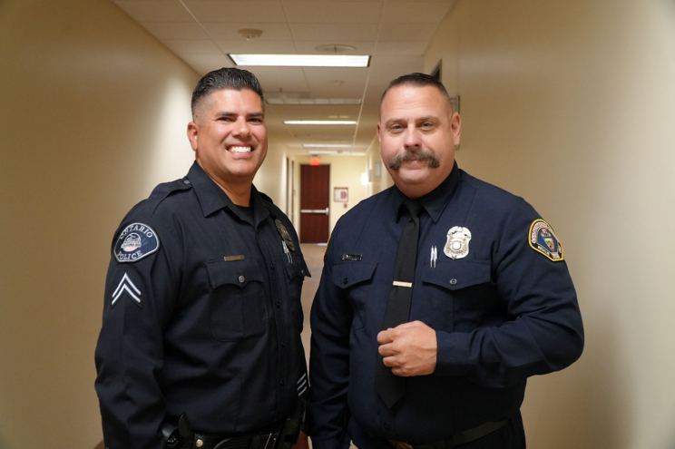 Two smiling officers pose for a photo in a hallway
