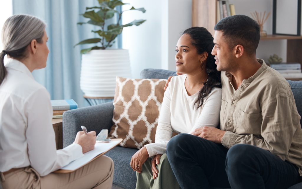 Young couple sitting on a sofa speaking to a person holding a clipboard