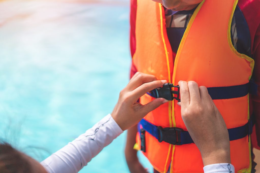Mother helping her child to wear life jacket before playing in swimming pool